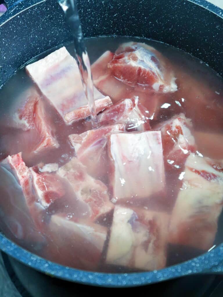 pouring water over pork spare ribs in a pot