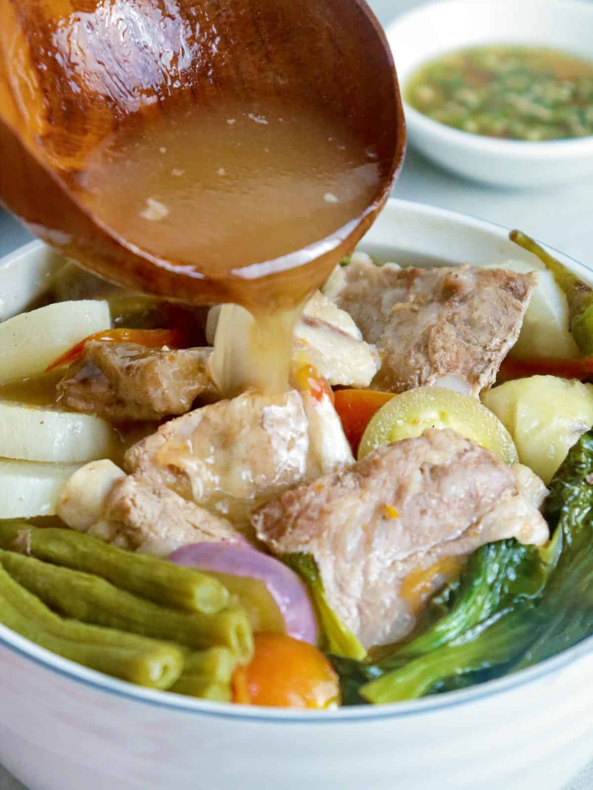 pouring broth in a bowl of sinigang na baboy