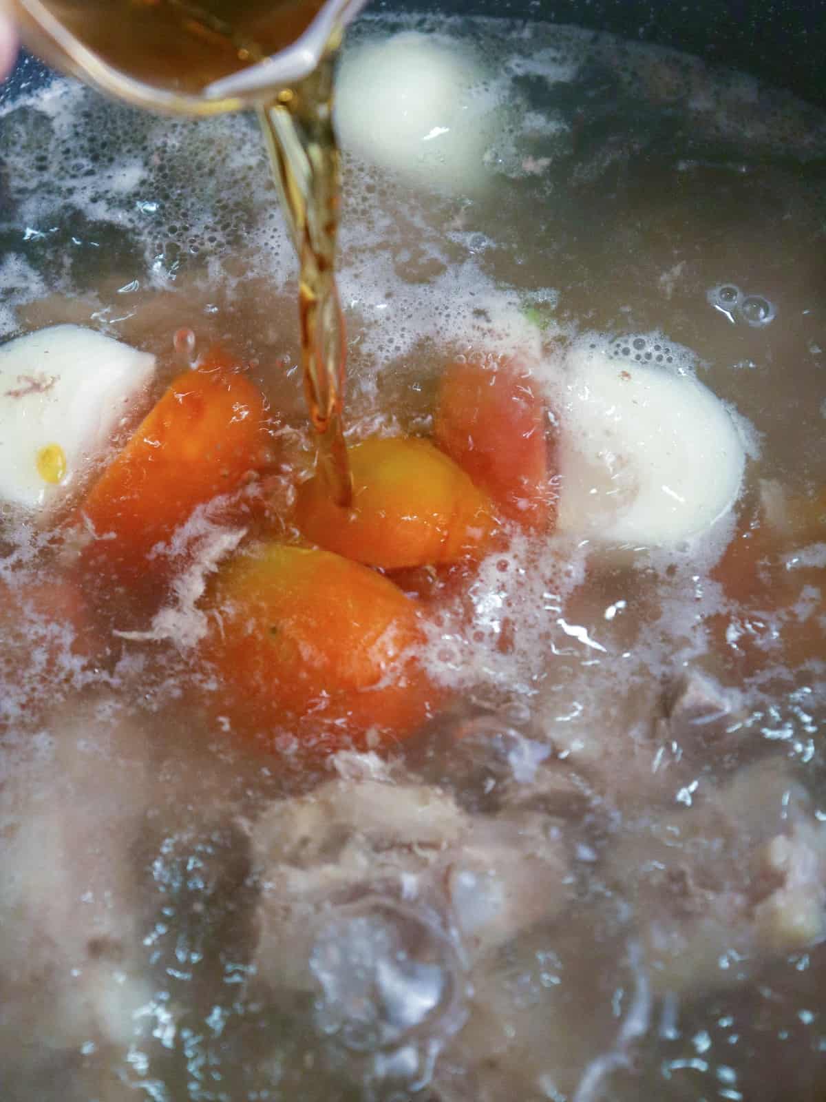 pouring fish sauce in a pot of pork soup