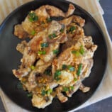 crispy fried frog legs with garlic butter sauce and scallions on a black plate