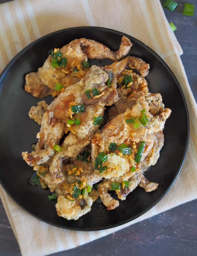 crispy fried frog legs with garlic butter sauce and scallions on a black plate