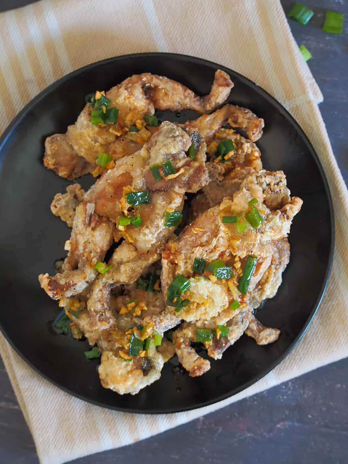 crispy fried frog legs with garlic butter sauce and scallions on a black plate