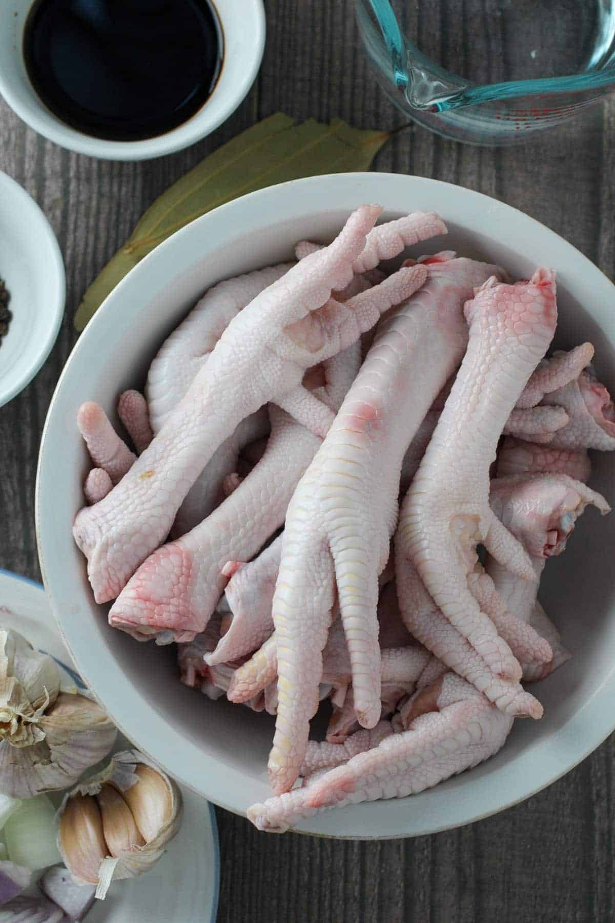 uncooked chicken feet in a bowl with bowls of soy sauce, garlic, and vinegar on the side