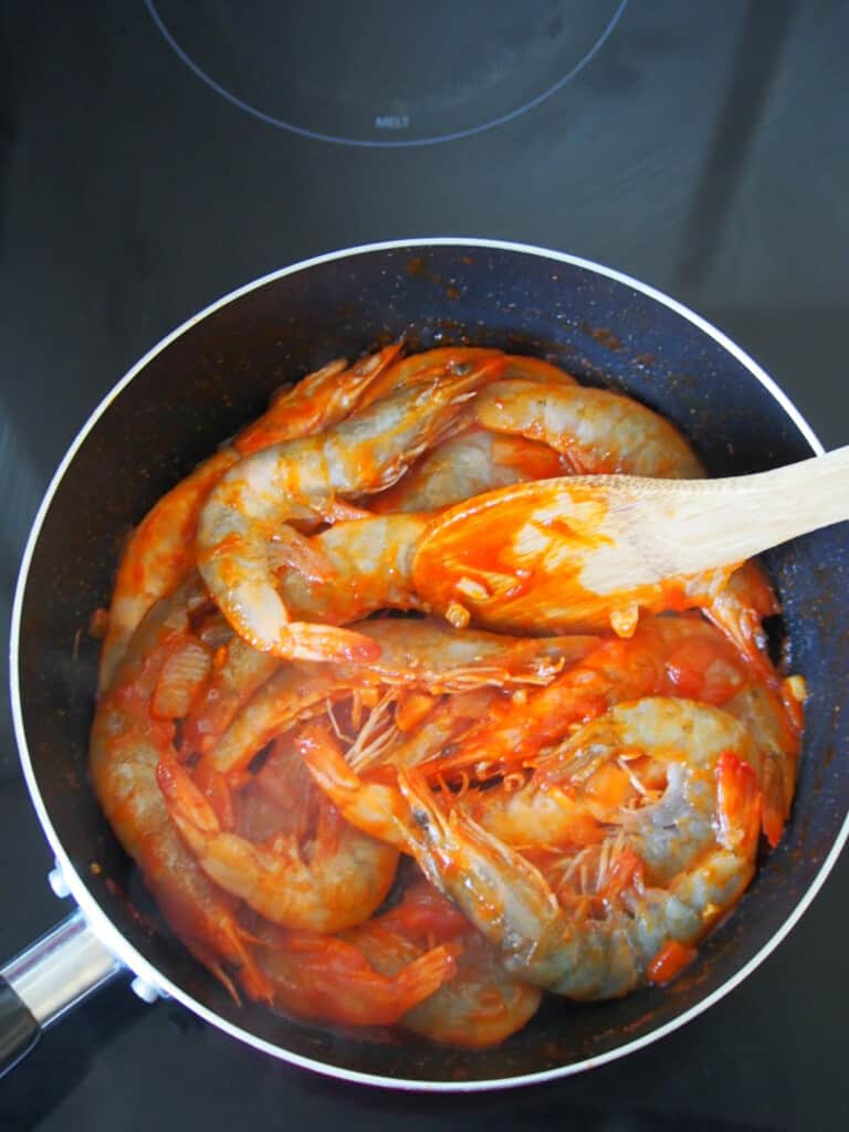 cooking shrimp in tomato and sauce in a pan