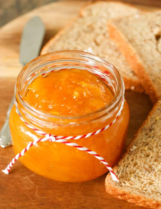 Mango Jam in a mason jar with wheat bread slices in the background.