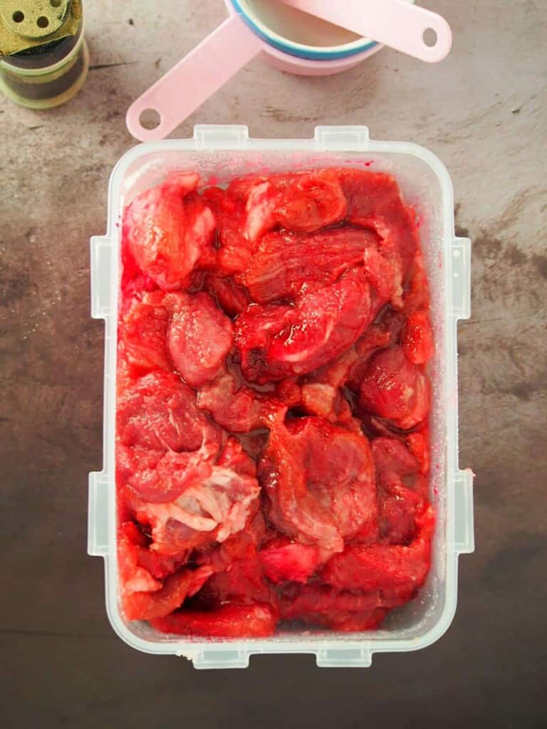 marinating sliced pork in sugar, garlic powder, pepper, and red food coloring in a plastic container