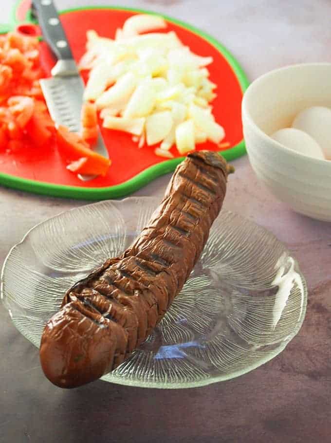 roasted eggplant on clear glass plate with eggs and chopped onions and tomatoes on the side
