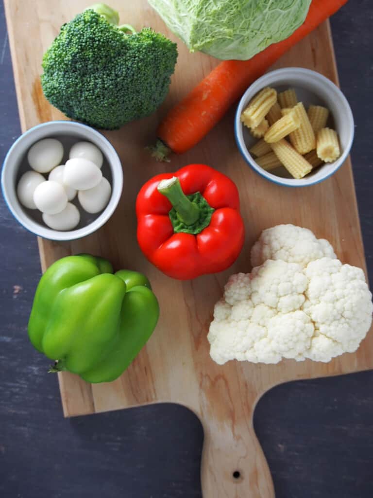 fresh cauliflower, broccoli, bell peppers, quail eggs, carrot, and baby corn on a cutting board
