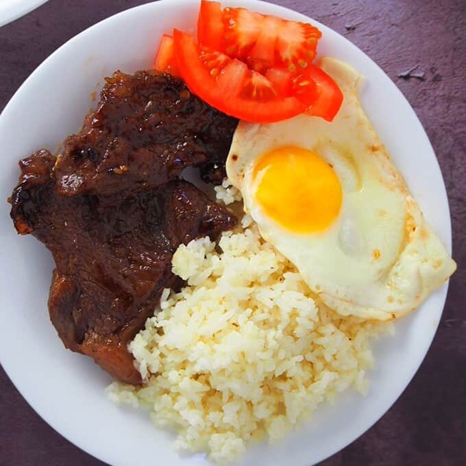 beef tapa with garlic fried rice and sunny side up eggs on a white plate