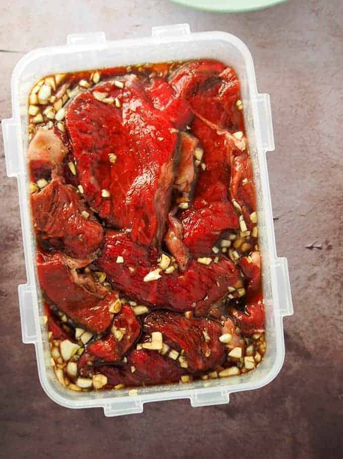 beef slices marinating in fish sauce, garlic, brown sugar, and pepper in a rectangle plastic dish