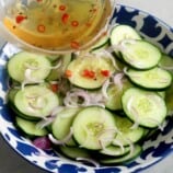 pouring vinaigrette over cucumber salad in a bowl