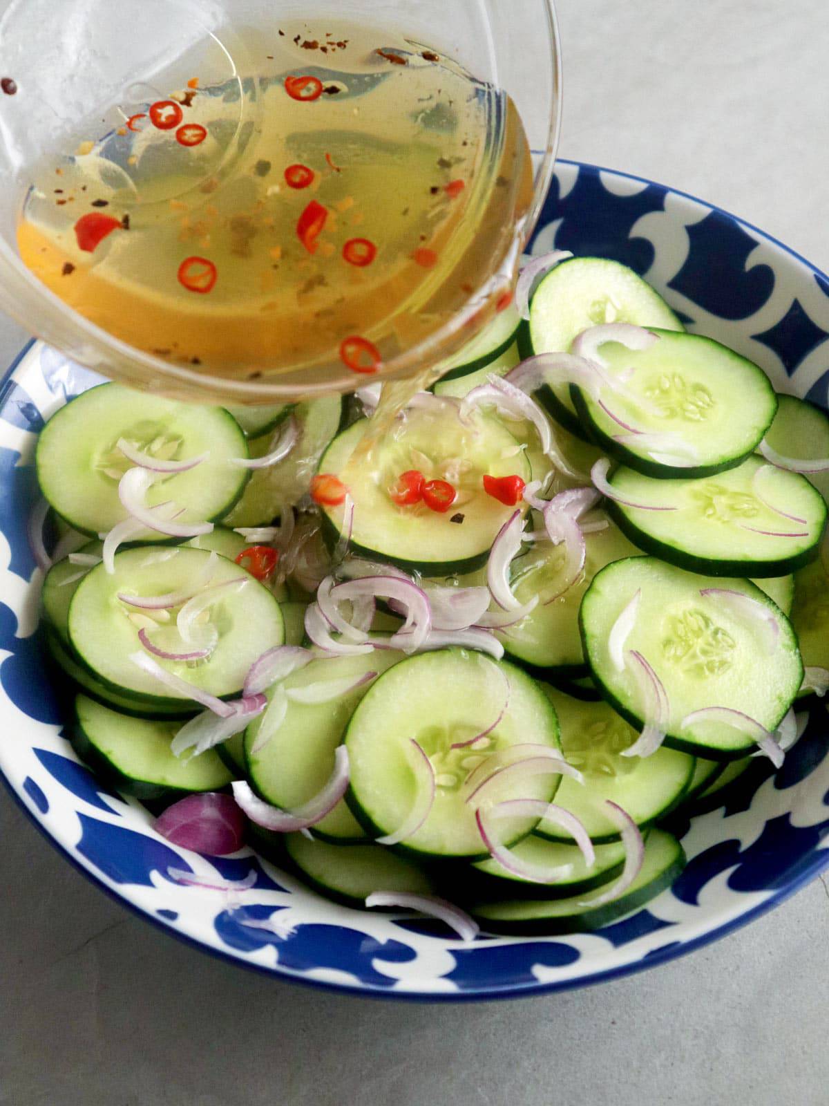 pouring vinaigrette over cucumber salad in a bowl
