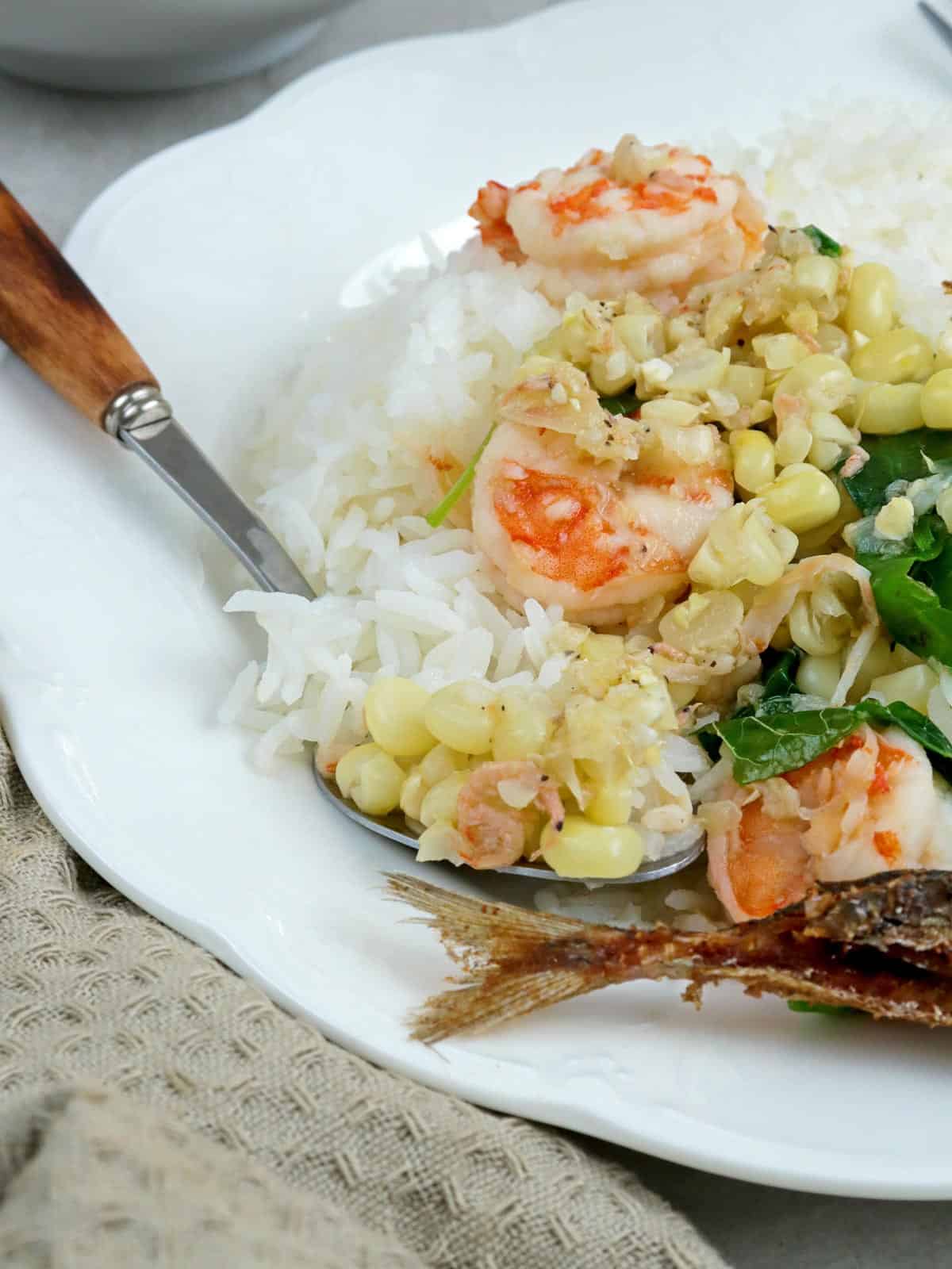 Filipino-style corn soup over rice steamed rice on a white plate