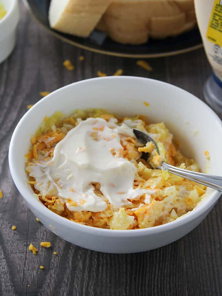 mixing mayonnaise, crushed pineapple, shredded cheese in a white bowl to make a spread