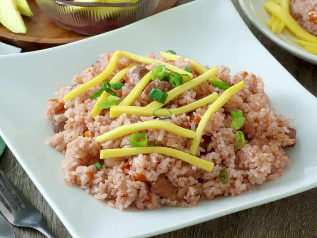 bagoong rice topped with julienned mangoes and green onions on a white serving plate