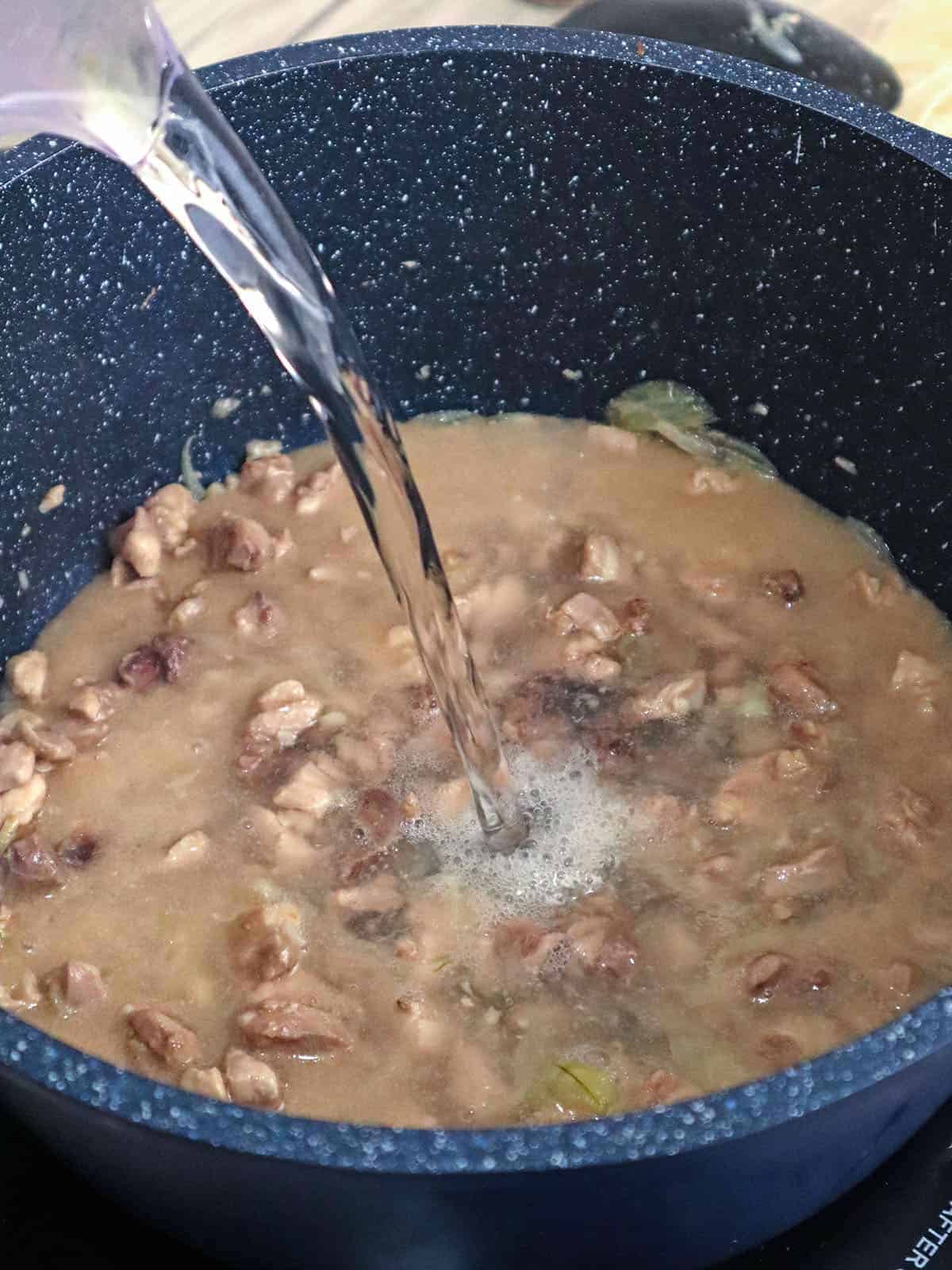 adding water to sauteed diced chicken thighs in pot