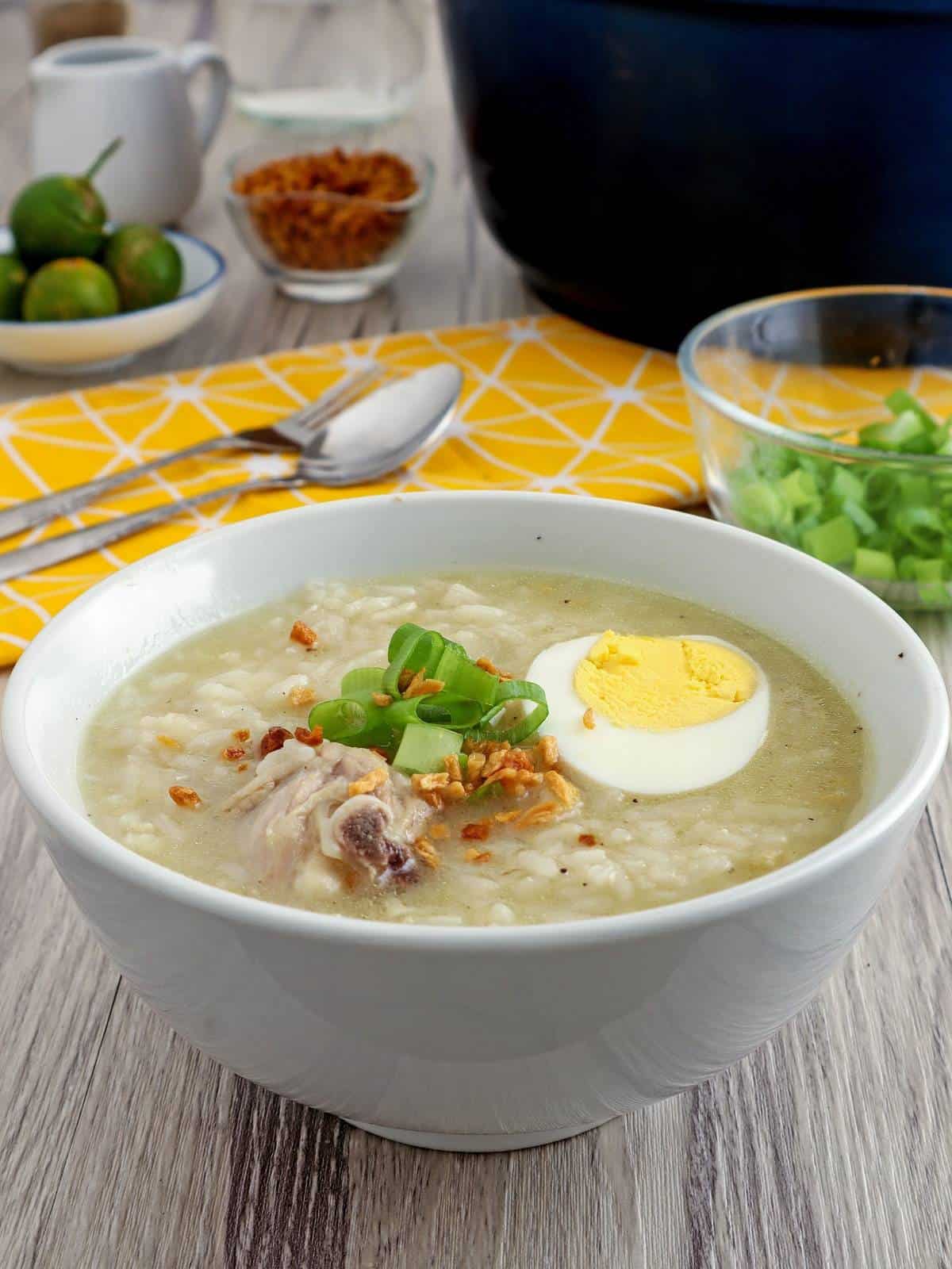 arroz caldong manok in a white serving bowl with hard boiled egg, green onions, and fried garlic bits on top