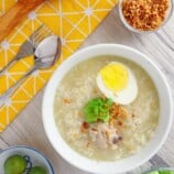 Chicken Arroz Caldo in white serving bowls topped with boiled egg, green onions, and fried garlic bits