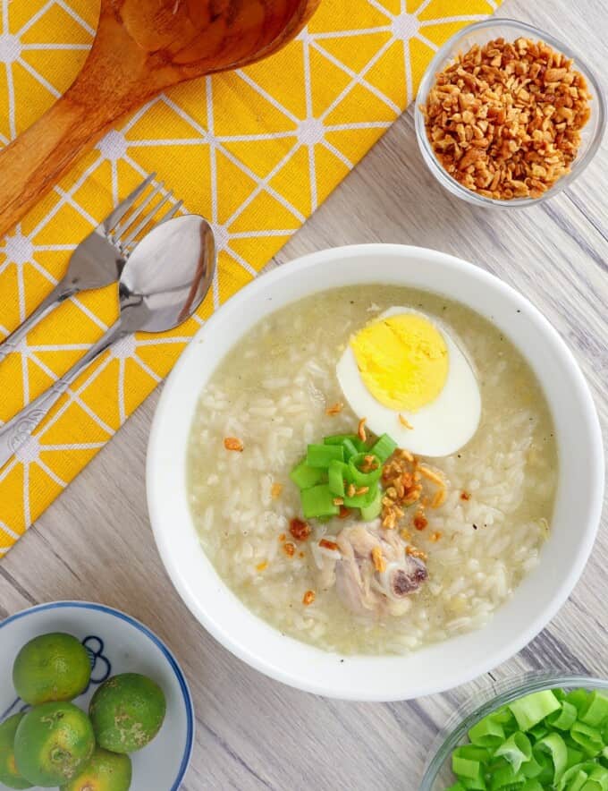 Chicken Arroz Caldo in white serving bowls topped with boiled egg, green onions, and fried garlic bits