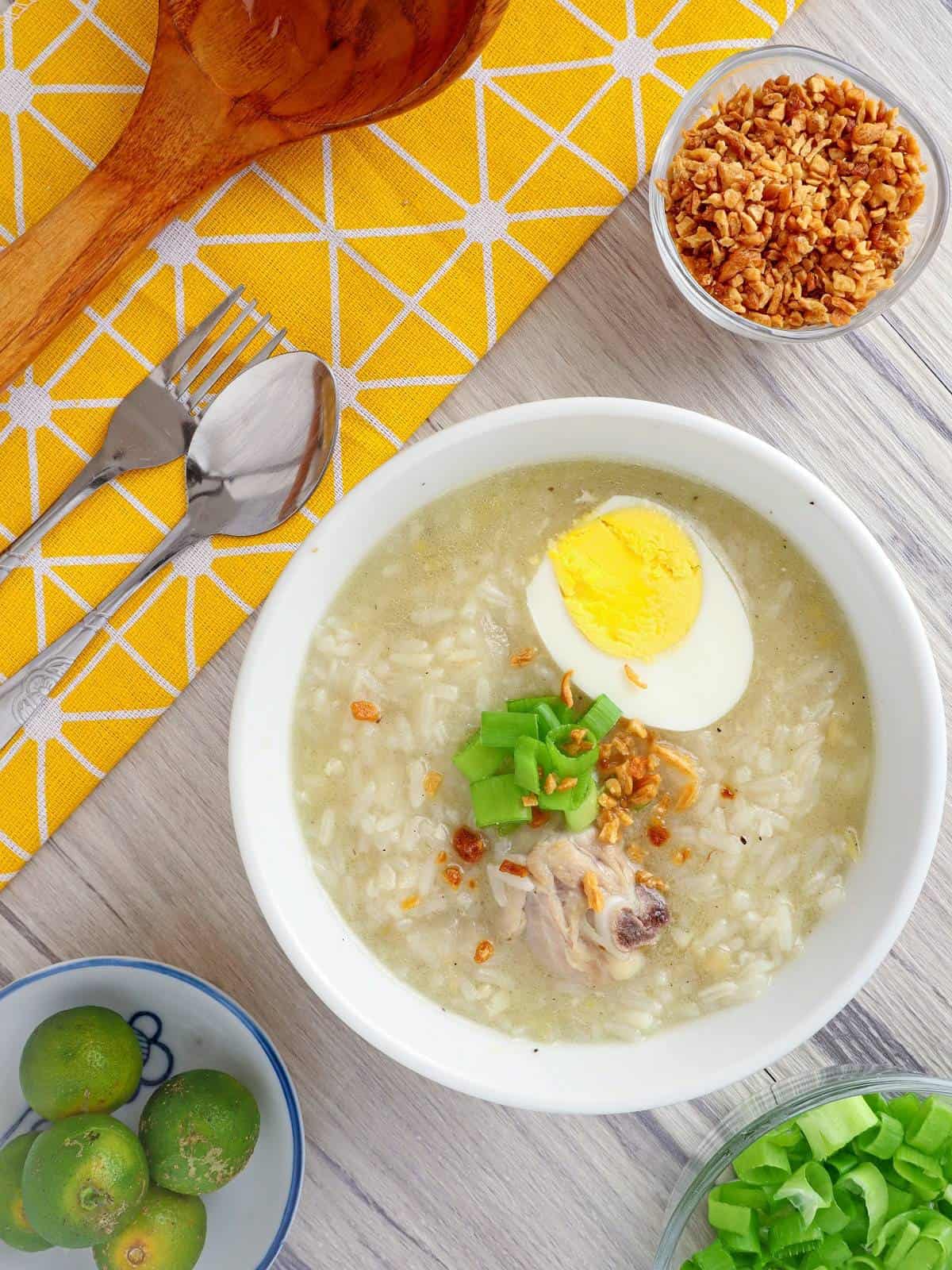 Chicken Arroz Caldo in white serving bowls topped with boiled egg, green onions, and fried garlic bits