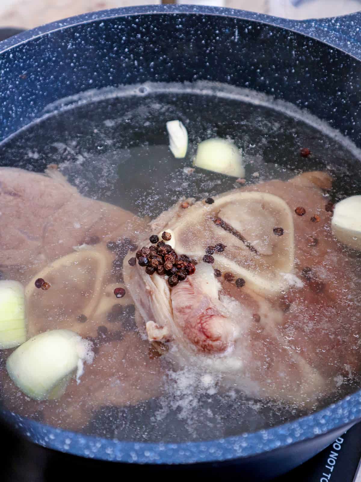 beef shanks in a pot of water with onions and peppercorns