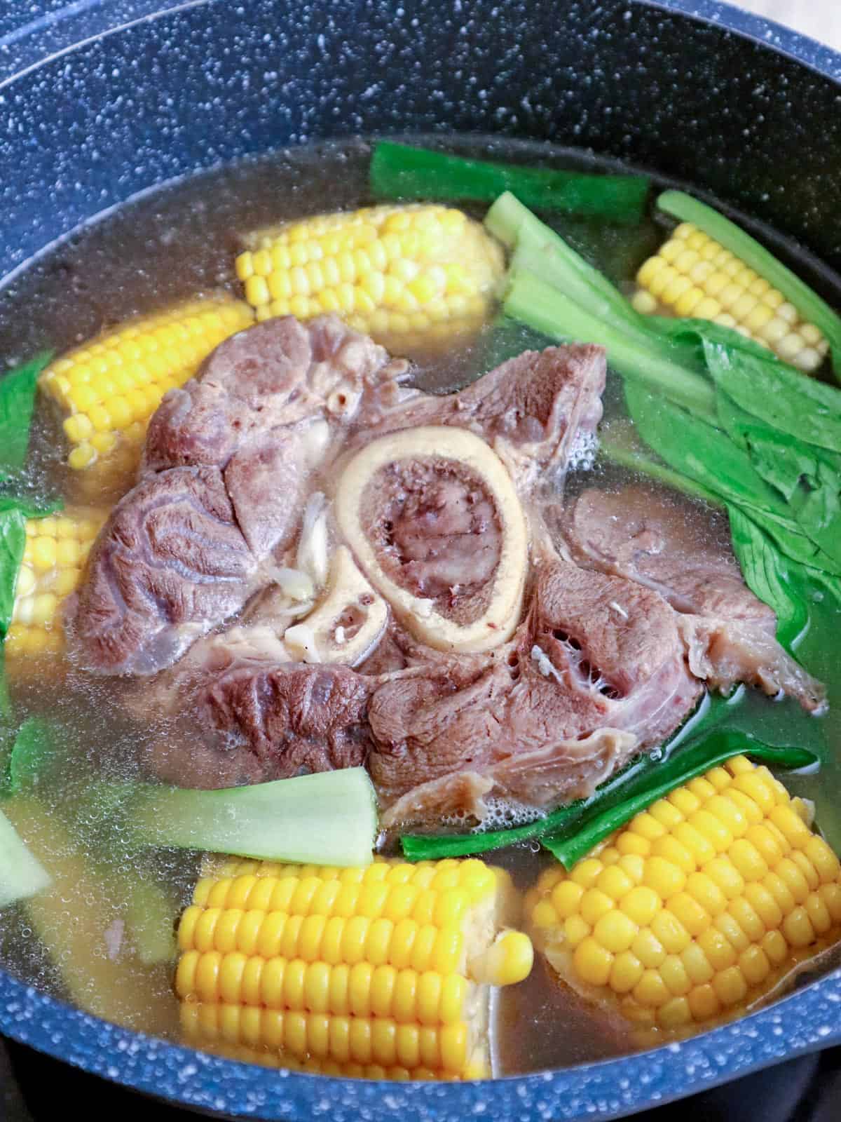cooking bulalo with corn, pechay, and green onions in a pot