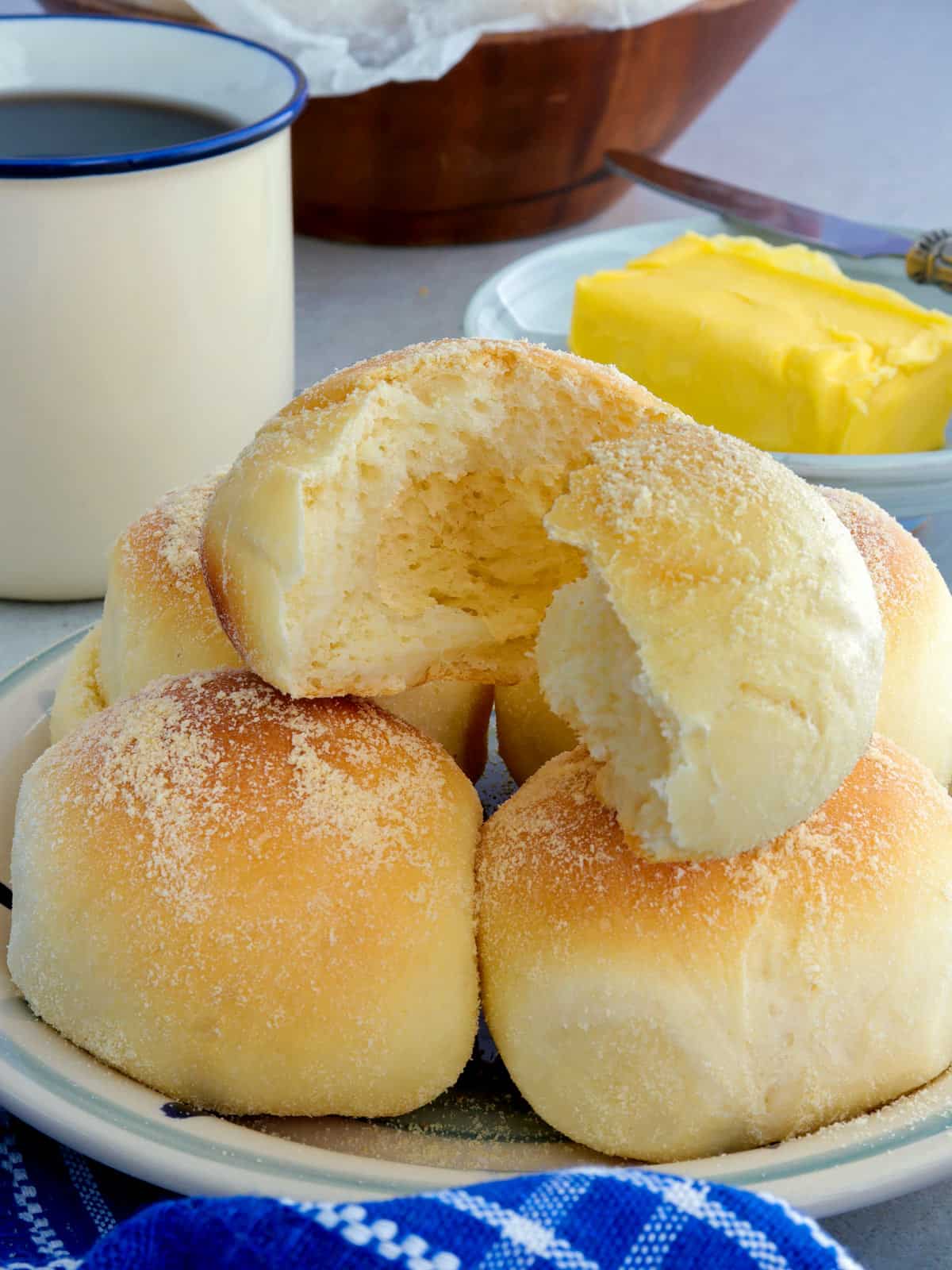 split pan de sal on a serving plate with a cup of coffee and a plate of butter on the side