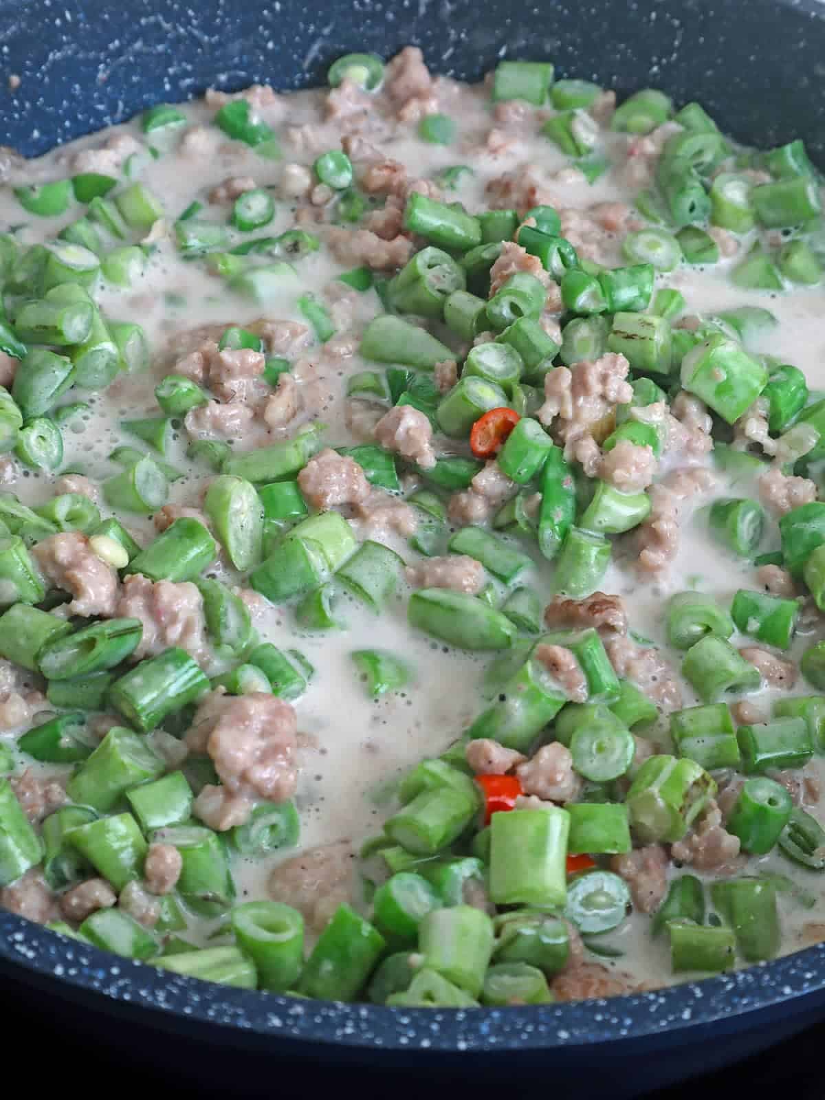 cooking green beans with coconut milk and ground pork in a skillet