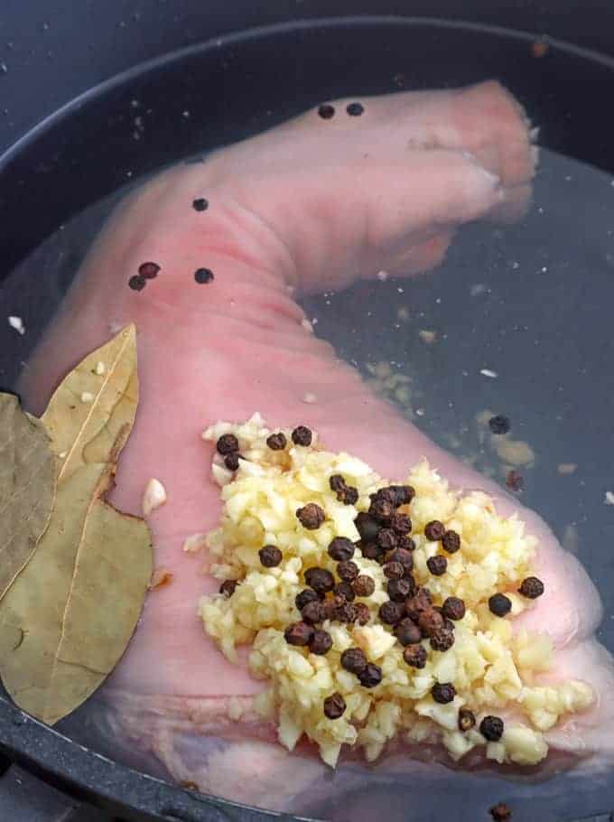 whole pork leg in a pot with vinegar, garlic, bay leaves, peppercorns ready to boil