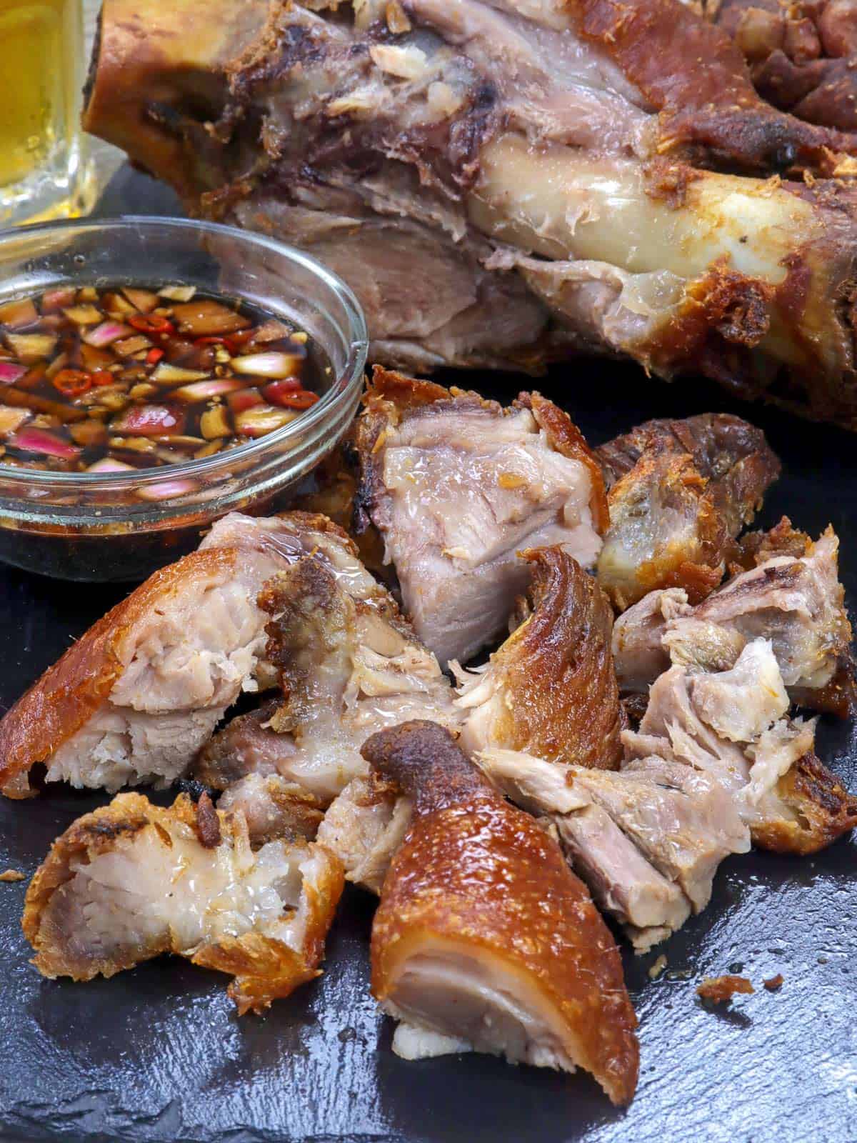 chopped crispy pata on a cutting board with sawsawan on the side.