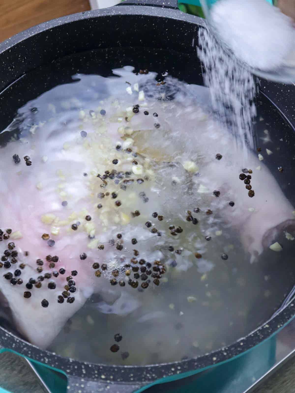 adding salt to whole pork leg in a pot with liquid and aromatics.