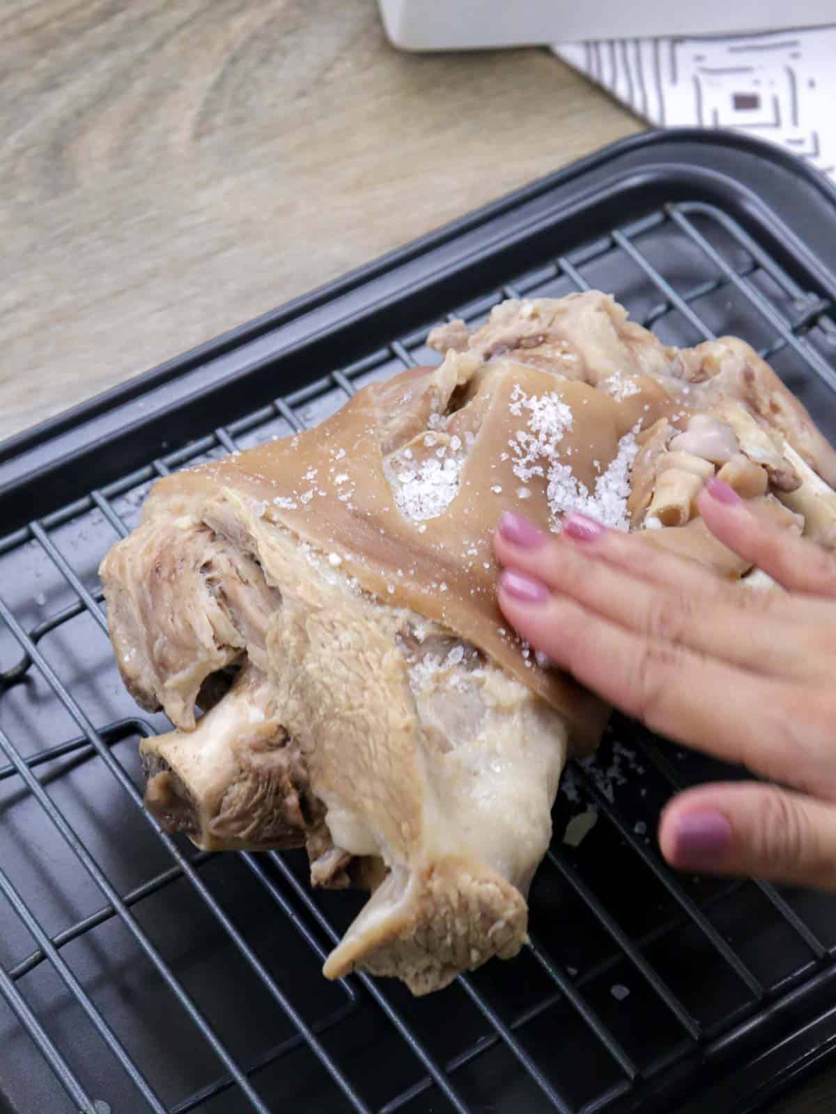 rubbing salt on boiled pork leg on a wire rack.