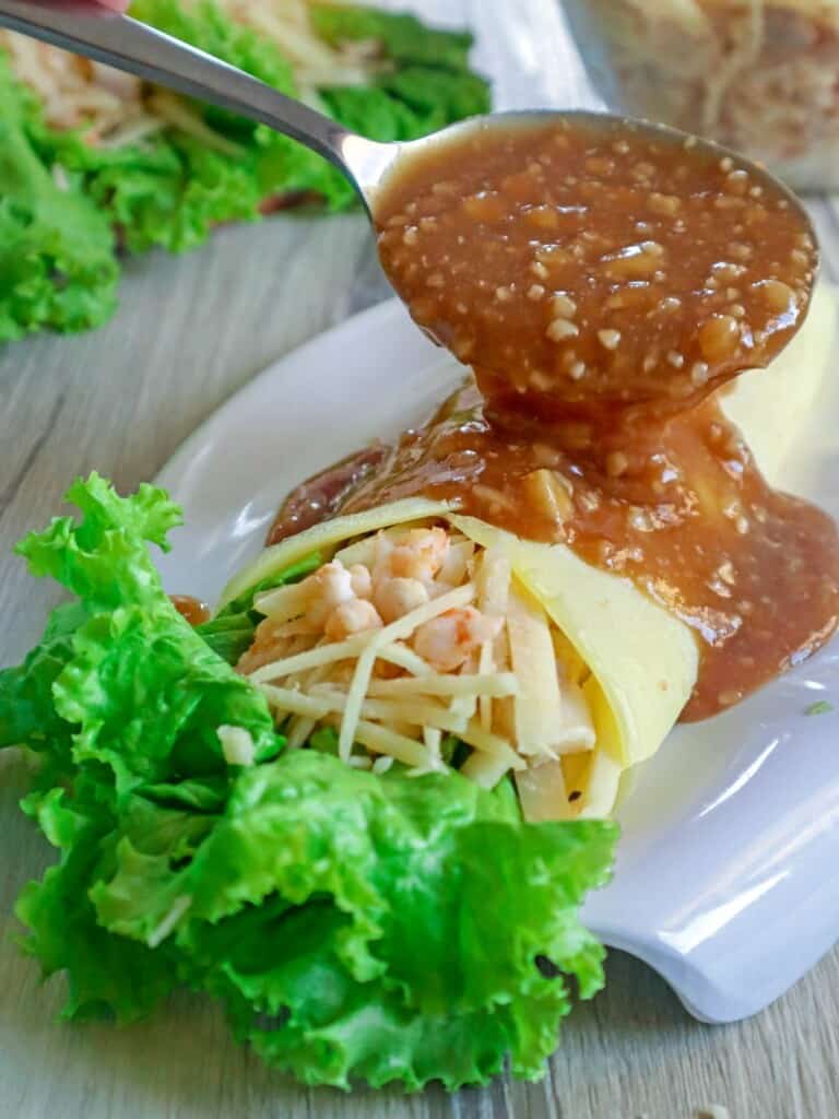pouring lumpia sauce over lumpiang ubod on a plate