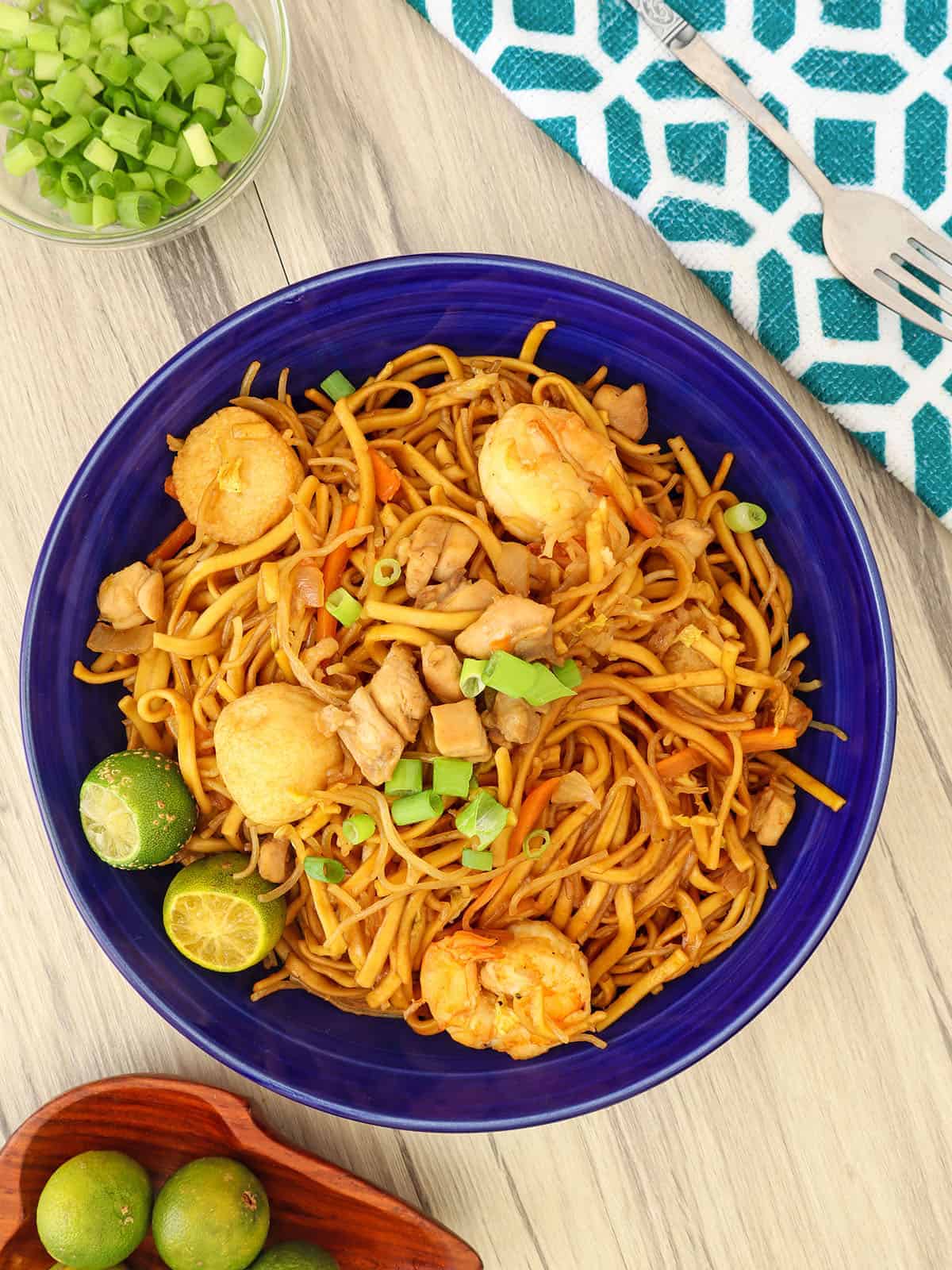 miki bihon in a blue serving platter with calamansi and chopped green onions on the side