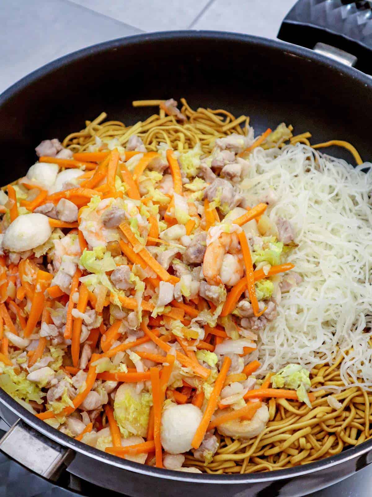 making miki bihon in a pan with chicken, shrimp, fish balls and veggies