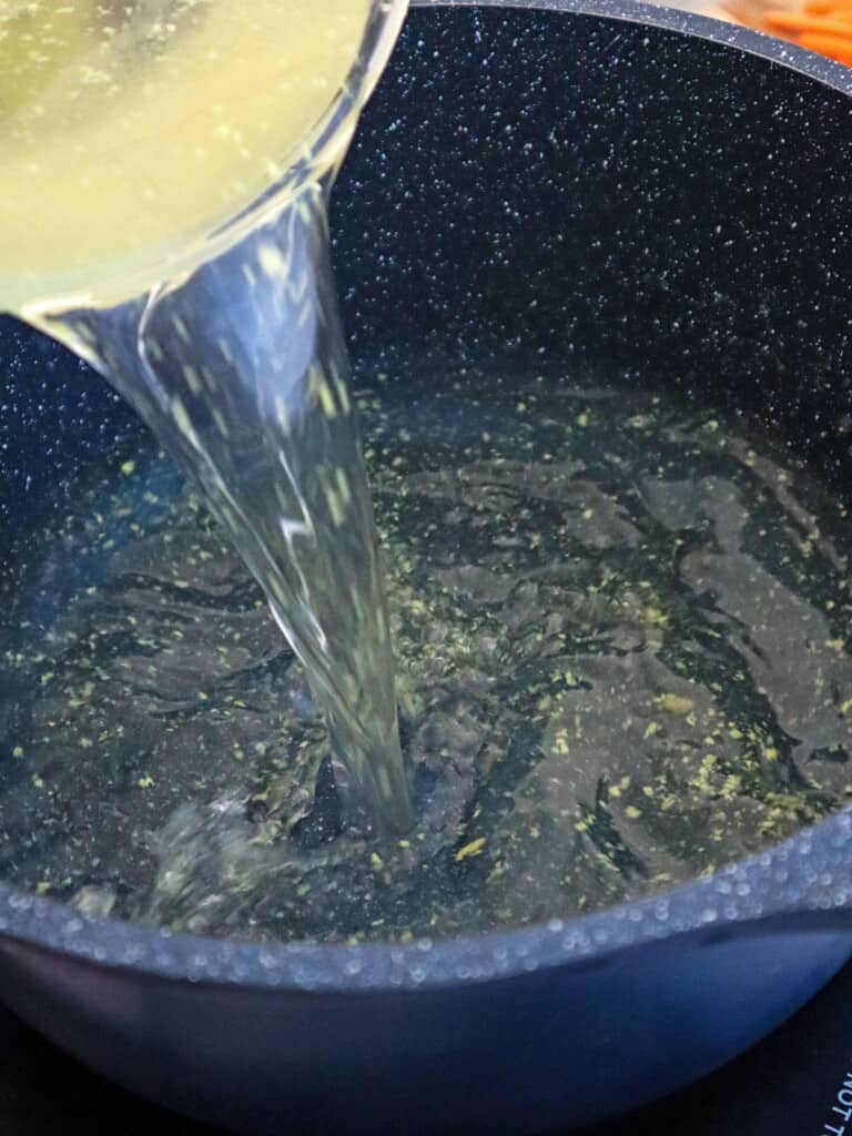 pouring chicken broth in a pot