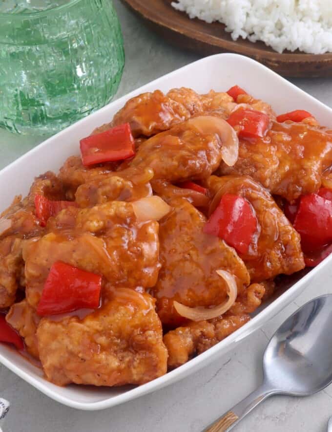 Sweet and Sour Fish in a white serving dish with a plate of steamed rice on the side