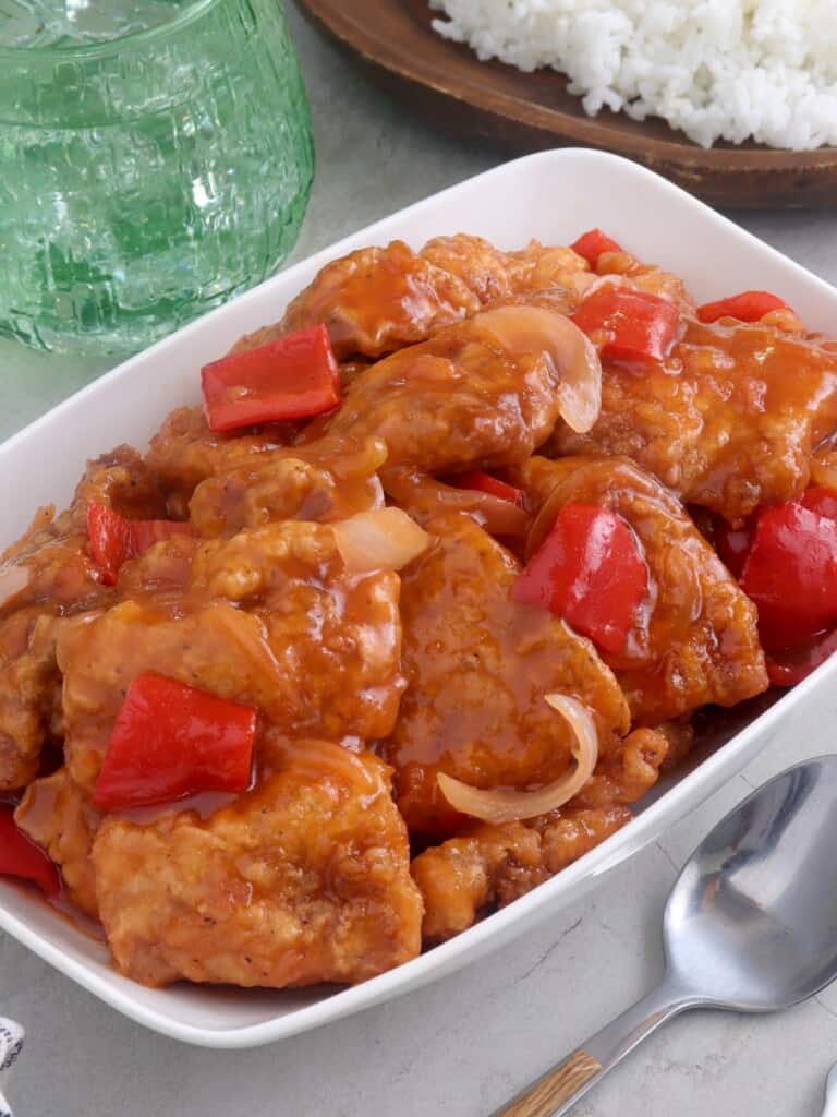 Sweet and Sour Fish in a white serving dish with a plate of steamed rice on the side