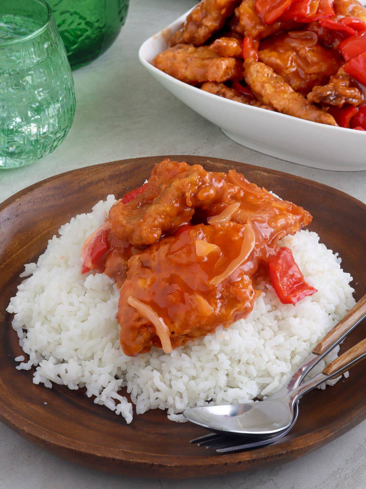 sweet and sour fish over steamed rice on a wooden plate