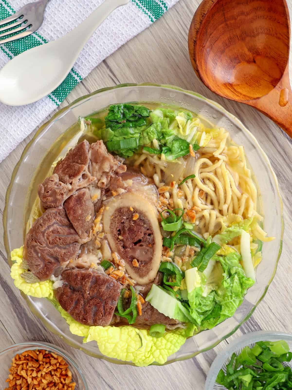 Bulalo Mami in a bowl with fried garlic bits and chopped green onions on the side