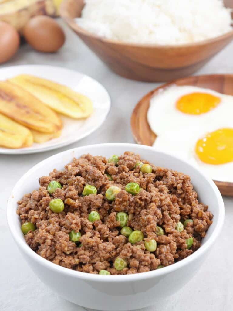 Arroz a la Cubana in a white serving bowl with fried saba, fried eggs, and steamed rice on the size