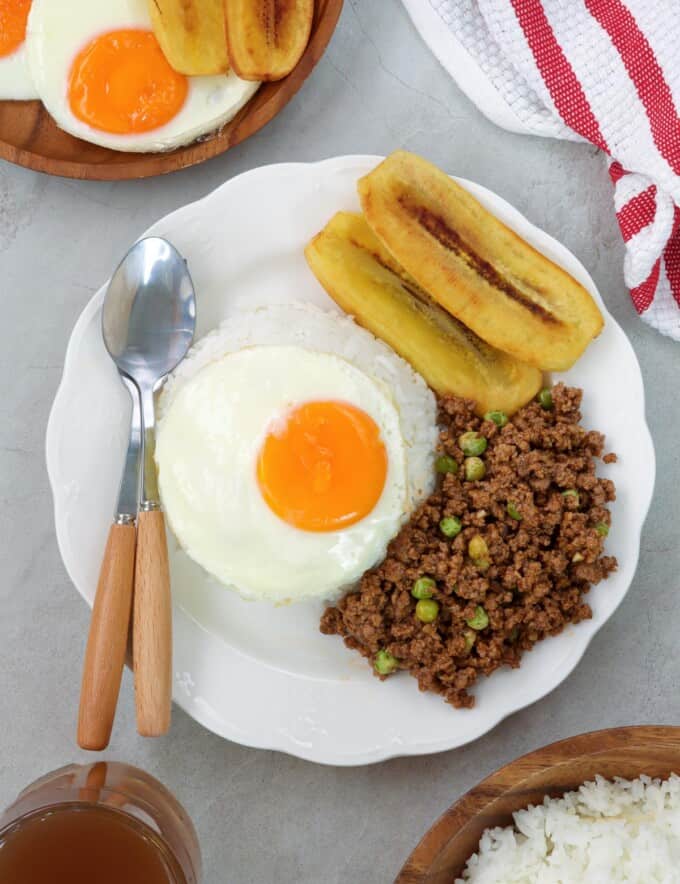 cuban rice with ground beef hash, fried egg, fried bananas, and white rice on white serving plate