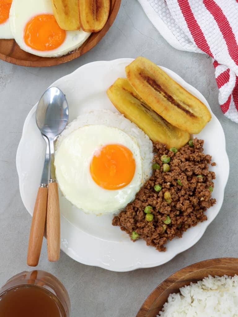 cuban rice with ground beef hash, fried egg, fried bananas, and white rice on white serving plate