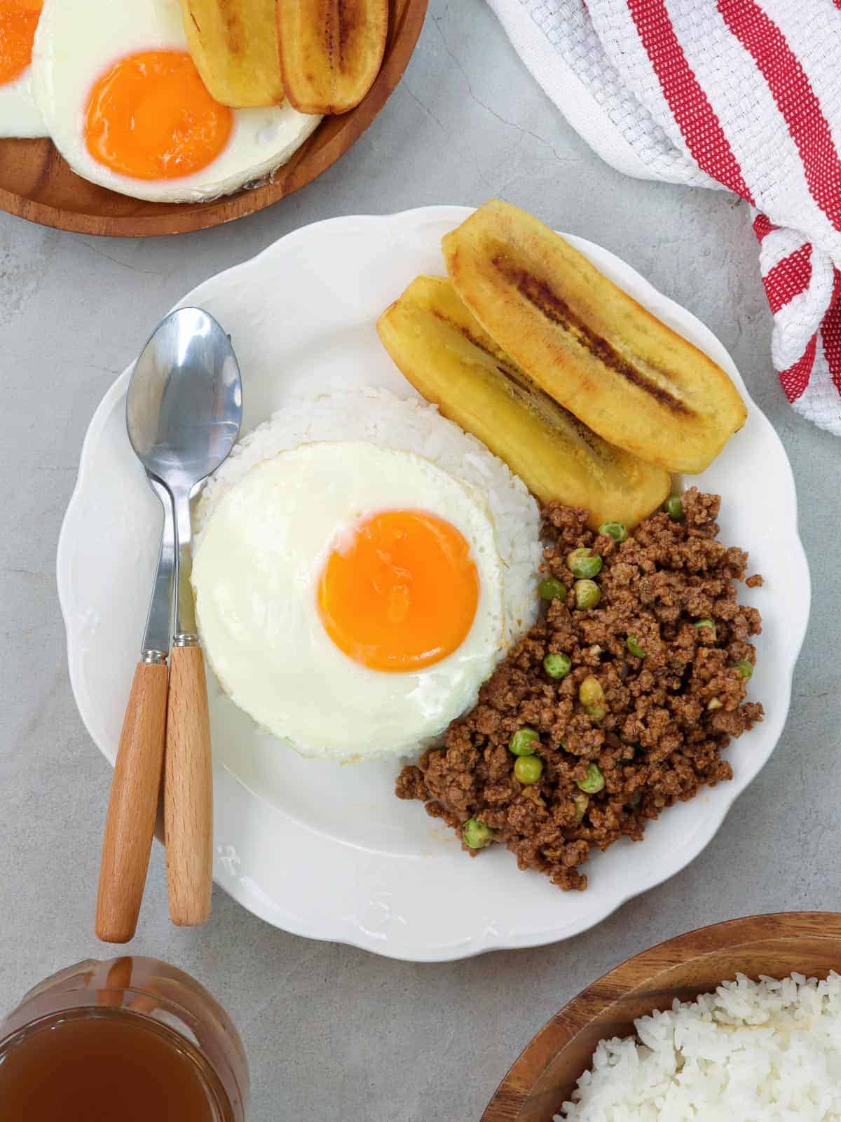 cuban rice with ground beef hash, fried egg, fried bananas, and white rice on white serving plate