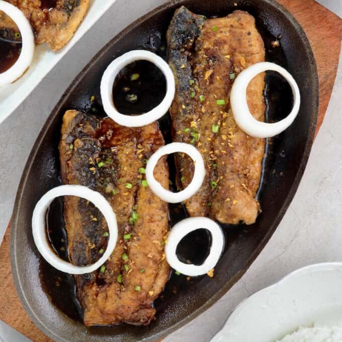 bangus a la pobre with onions and crispy garlic on a sizzling plate