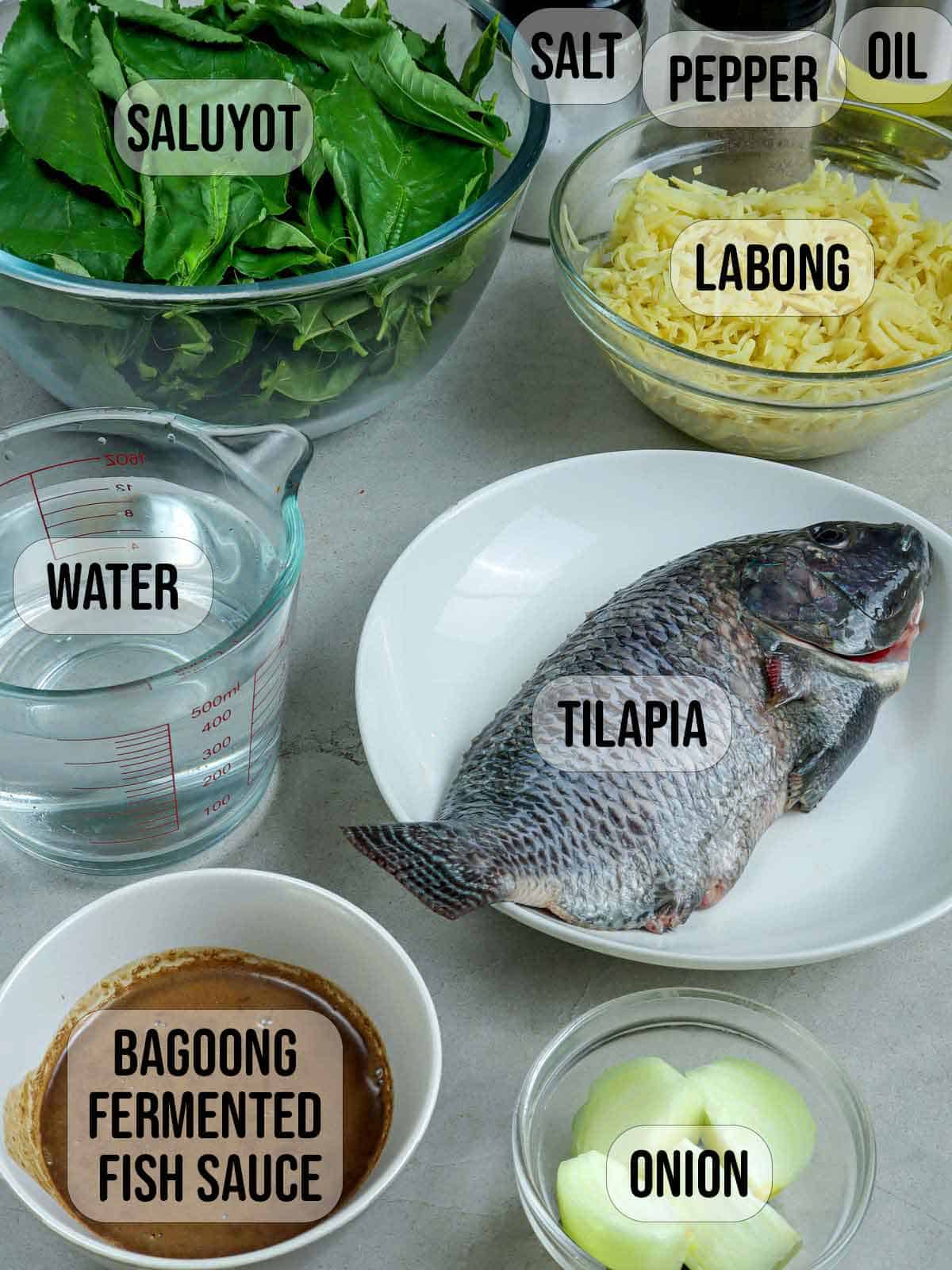 tilapia, onion, bamboo shoot, jute leaves, water, bagoong isda, oil in bowls, and salt and pepper shakers in the background.