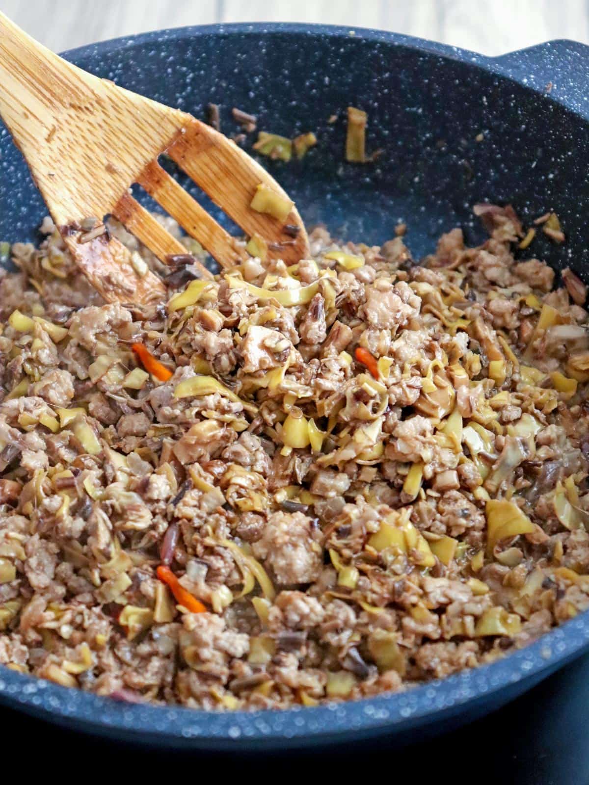 stirring sauteed banana hearts with pork in a pan with a wooden spoon