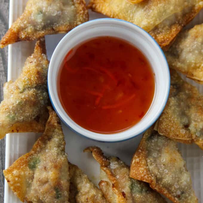 fried wontons on a serving platter with a bowl of sweet and sour dipping sauce