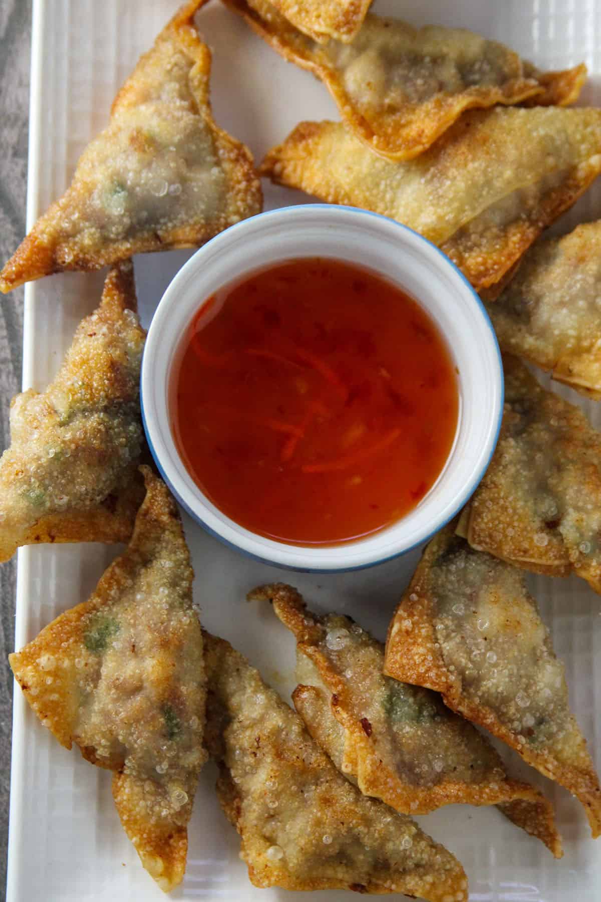 fried wontons on a serving platter with a bowl of sweet and sour dipping sauce