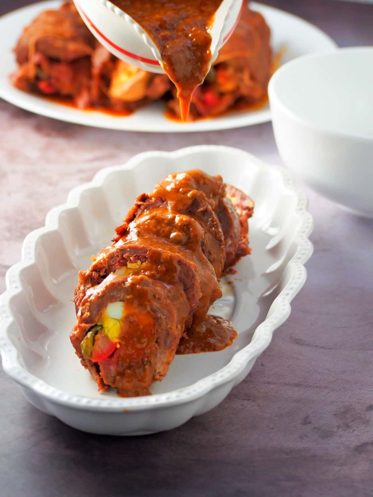 drizzling tomato gravy over sliced beef morcon in a serving dish